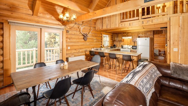 L’intérieur d’une cabane en rondins comprend un coin repas, une cuisine et un grand plafond en bois.
