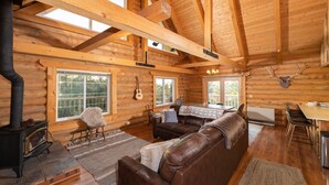 L’intérieur d’une cabane en rondins, avec une cheminée, un canapé en cuir, une table à manger et une tête de cerf accrochée au mur.
