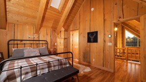 Une chambre dans une cabane en bois, avec un lit, un luminaire au plafond et une porte donnant sur un balcon.