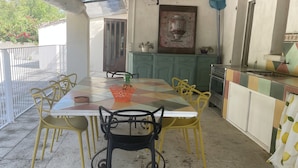 Eine Terrasse im Freien mit Fliesenboden, einem Tisch mit Stühlen, einem Grill und einem Schrank.