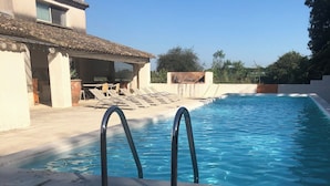 Ein Schwimmbecken mit zwei Metallleitern, einem Ziegeldach und einem Gebäude mit Balkon im Hintergrund.