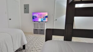 A hotel room with two beds, a TV on a stand, a wardrobe, and a door. - Tiki 1 Bedroom Home by RedAwning (South Padre Island)