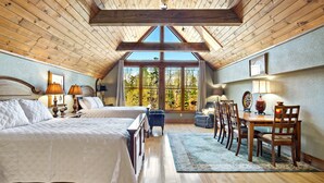 Un espacioso dormitorio con dos camas, una zona de comedor con muebles de madera y ventanas amplias que dan a vistas de árboles.