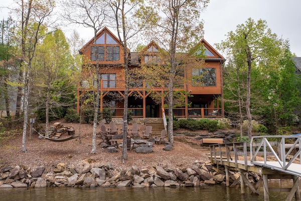 A stunning lakefront home nestled among lush greenery, featuring expansive windows and multiple decks that offer panoramic views of Lake James.