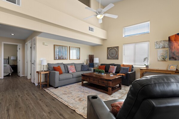 A spacious living room with a high ceiling, a ceiling fan, a fireplace, and a large window with blinds. - About Time Oasis Mesquite Vacation Rental with Private Balcony with $510 of free daily activities (Mesquite)