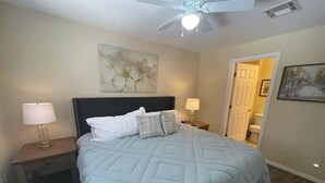 Una camera da letto con un letto, comodini, una ventola a soffitto e una porta che dà su un bagno.
