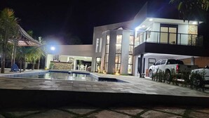 Uma casa moderna de dois andares com piscina, área de estar externa e garagem com veículos.