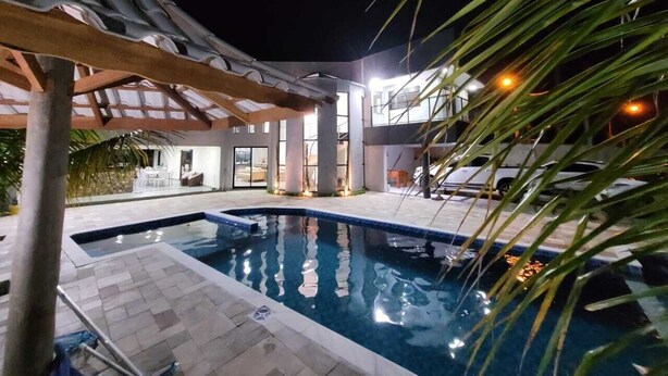 Piscina interna com deck ladrilhado, área de estar coberta e vista para o edifício vizinho.