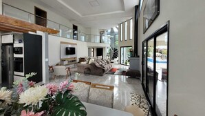 Ampla sala de estar com uma TV grande, assentos confortáveis, uma escada e vista para o exterior.