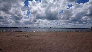 Ein Strand mit sandigem Ufer und einem Gewässer unter einem bewölkten Himmel.