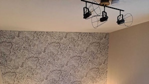 Ein Schlafzimmer mit blumengemustertem Wandpapier, einem Bett mit vielen Kissen, zwei Nachttischlampen und einer Deckenleuchte.