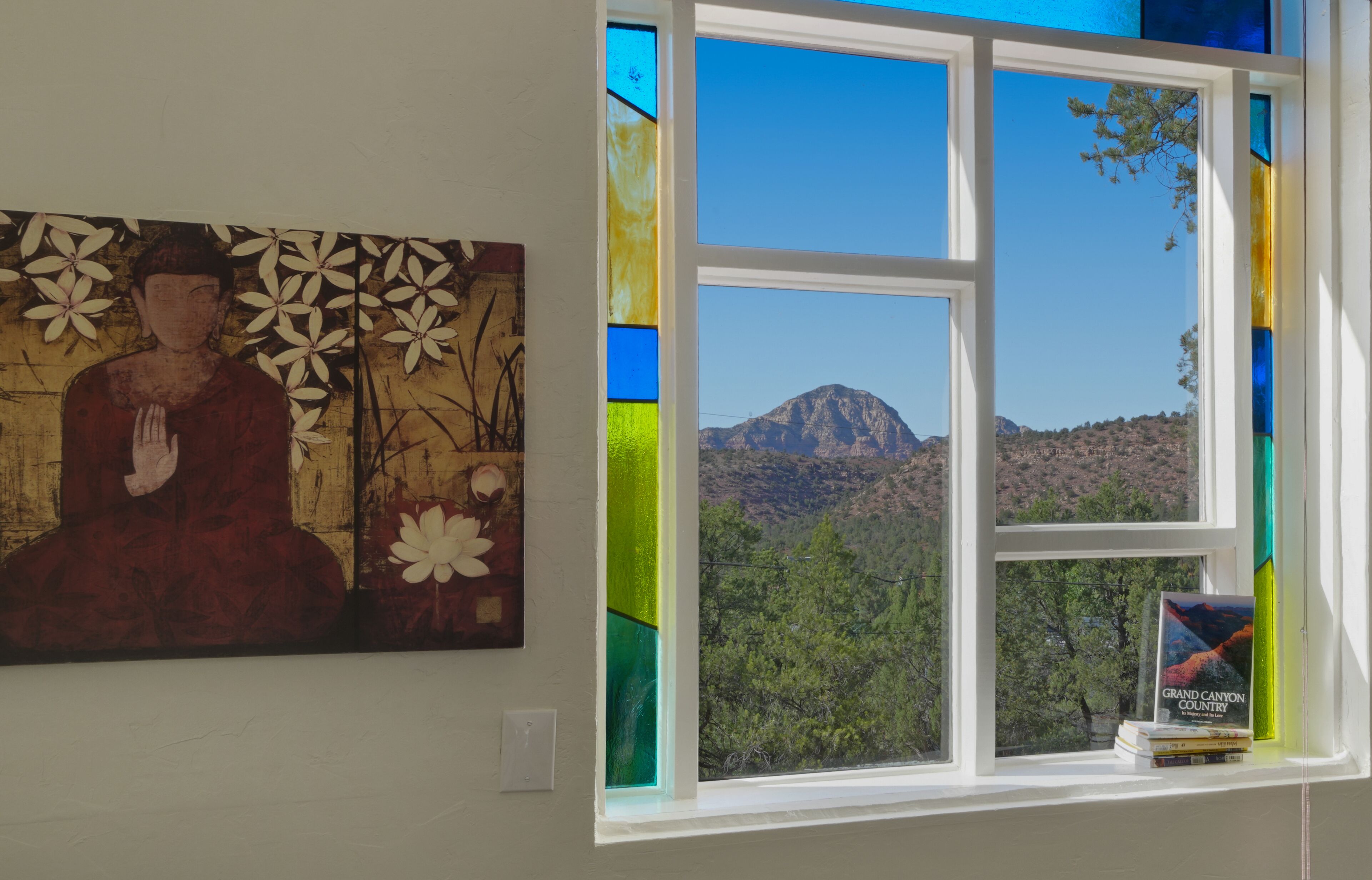 A room with a window overlooking a mountainous landscape, a Buddha painting on the wall, and a book titled "Grand Canyon Country" on the windowsill.
