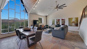 A spacious living room with a large dining table, comfortable seating, a fireplace, and large windows offering a scenic view. - Walk to Trails! Red Rock Views! Pet Friendly! (Sedona)