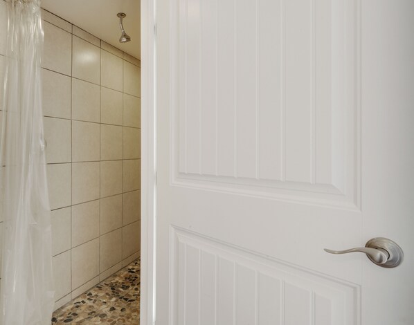 Une salle de bain avec des murs recouverts de carreaux blancs, un rideau de douche et une pomme de douche.