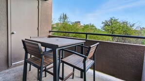 Un balcón con una mesa, sillas, una puerta y vistas a zonas verdes y edificios.