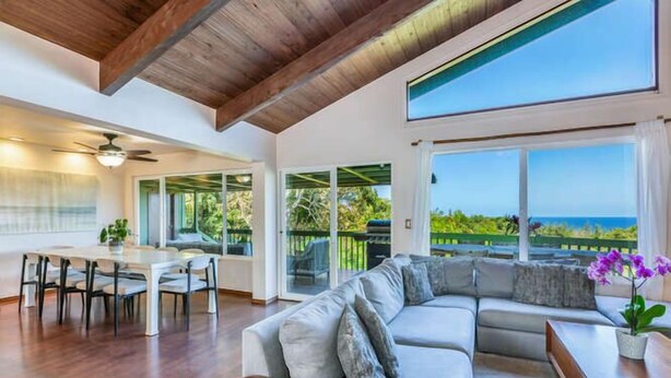 A spacious living area with a large sofa, a dining table, and a view of the ocean. - Hale Ohia: Secluded Home w/ Private Pool, Ocean & Mountain Views, BBQ (Princeville)