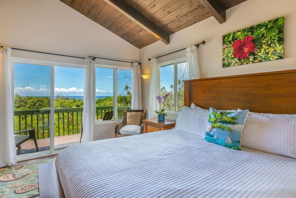 A bedroom with a large bed, a view of the ocean, and a wooden ceiling.
