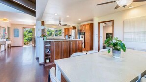 A spacious kitchen with wooden cabinets, a dining table, and a ceiling fan. - Hale Ohia: Secluded Home w/ Private Pool, Ocean & Mountain Views, BBQ (Princeville)