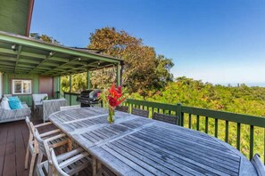 Eine Terrasse im Freien mit Holztisch und -stühlen, einem Grill und Blick auf eine üppige Landschaft.