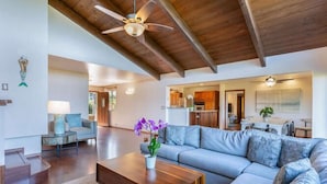 A spacious living room with a wooden ceiling, a large grey sofa, a wooden coffee table, and a ceiling fan. - Hale Ohia: Secluded Home w/ Private Pool, Ocean & Mountain Views, BBQ (Princeville)
