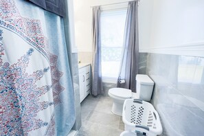 A bathroom with a toilet, a washing machine, and a window with curtains.