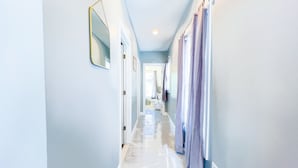A hallway with light blue walls, a marble floor, and a door leading to a bathroom. - The Cedar Chateau (Niagara Falls)