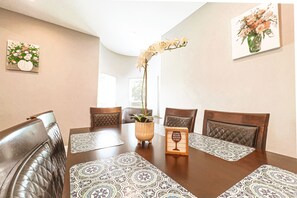 A dining area with a wooden table, patterned placemats, leather chairs, a vase with flowers, and a framed quote on the table.