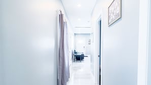 A bright, narrow hallway with light blue walls and a shiny tiled floor, leading to a room with a bed and a desk. - The Cedar Chateau (Niagara Falls)