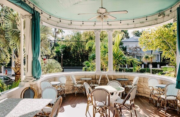 Relax in a serene outdoor space surrounded by lush greenery and palm trees, with comfortable seating and a stylish, curved ceiling.