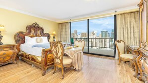 A spacious hotel room with a large bed, a dining area, and a balcony with a city view.