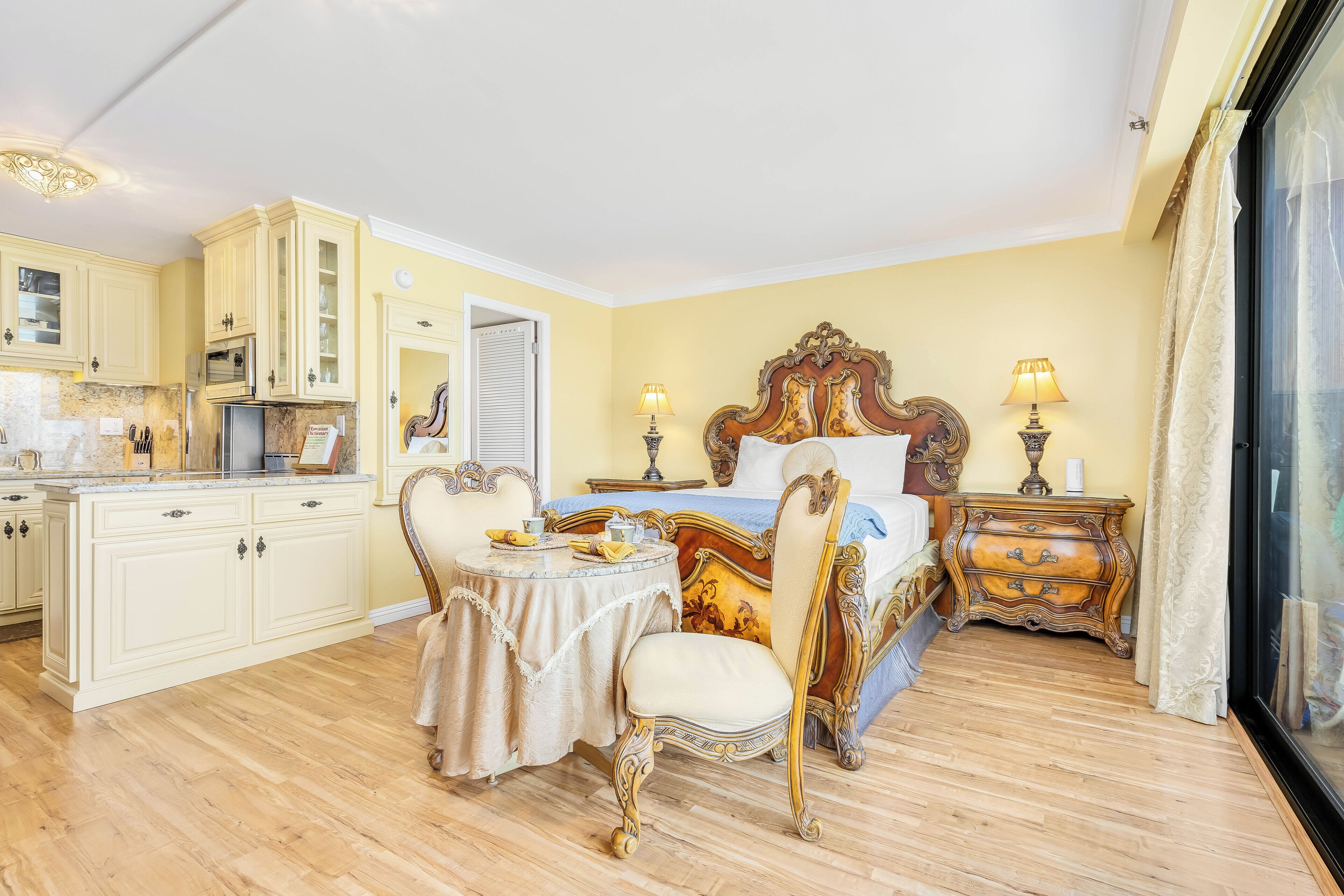 A room with a bed, a bedside table, a chair, a small table with a lamp, and a cabinet.