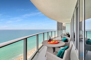 A balcony with a round table, wicker furniture, and a view of the beach and ocean. - Insane Ocean View Balcony |Beachfront Resort+Pools (Hollywood)