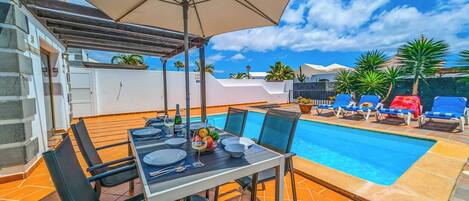 A poolside area with a dining table and chairs, a pool, and lounge chairs.