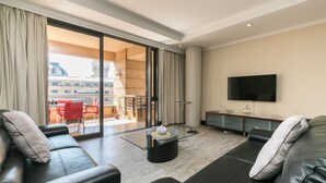 A modern living room with a glass coffee table, leather sofas, a flat-screen TV, and a sliding glass door leading to an outdoor dining area. - Raphael Penthouse | Square and Mall and Pool Access (Johannesburg)
