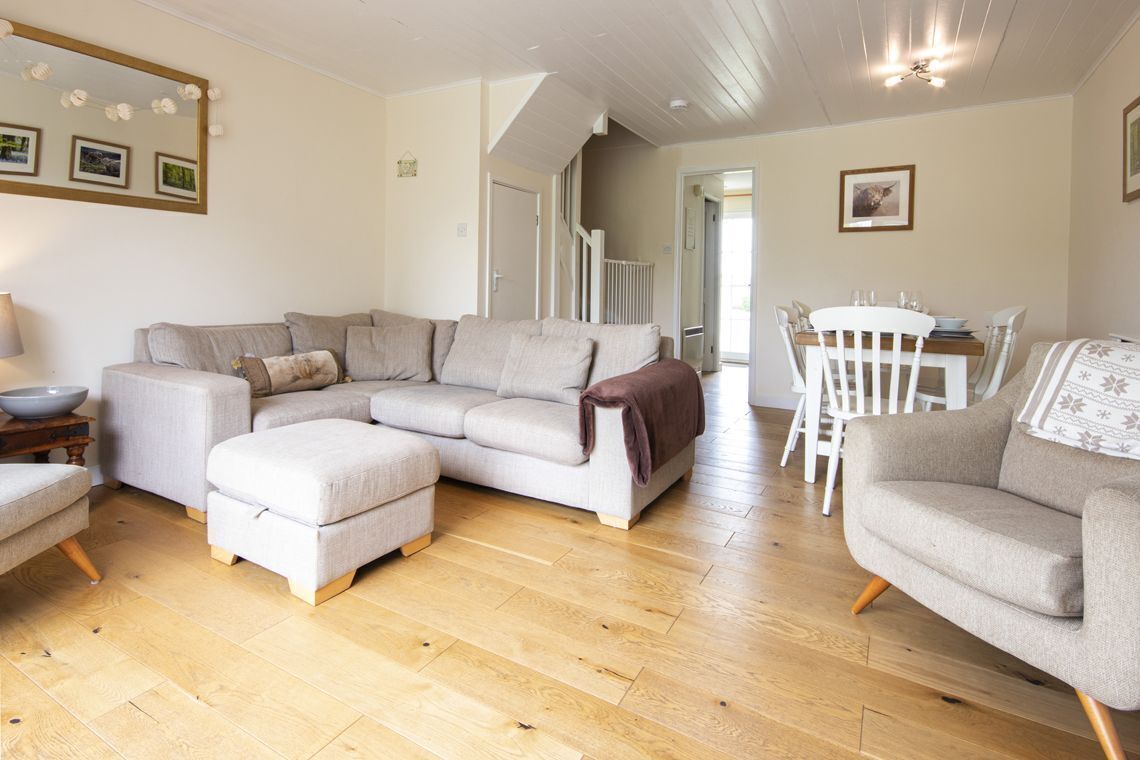 A spacious living room with a large L-shaped sofa, a small round table, and a dining table with chairs.