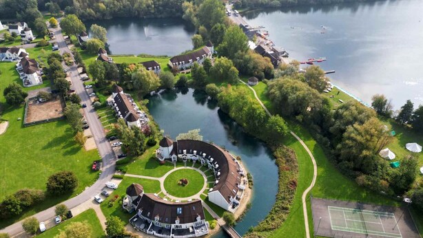 Luchtbeeld van een woongebied aan het water, met huizen, een tennisbaan en een rond park.