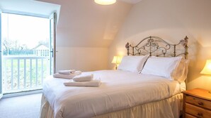 Een slaapkamer met een bed, twee bedlampen, een houten nachtkastje en uitzicht op een balkon.