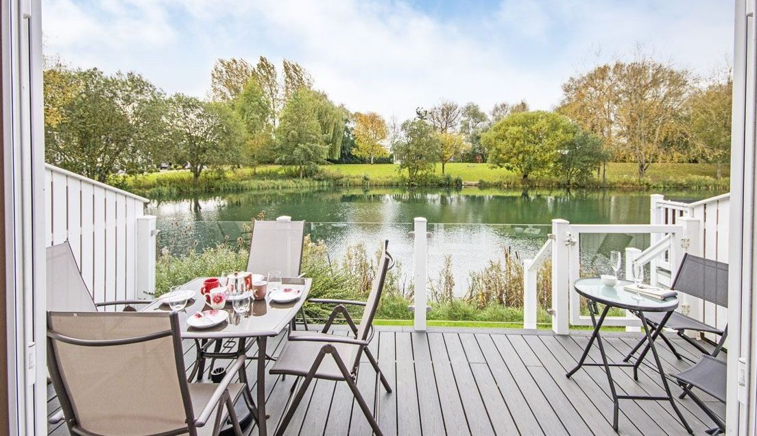 A deck with a table set for dining, overlooking a lake with trees in the background.