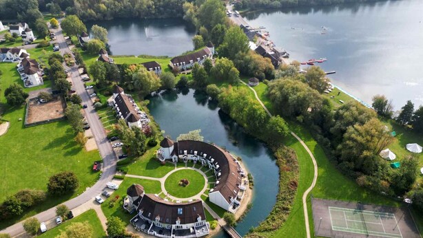 Vista aerea di una zona residenziale sul lago, con case, un campo da tennis e un parco circolare.