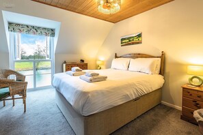 A bedroom with a bed, a chair, a nightstand, a lamp, and a painting on the wall.