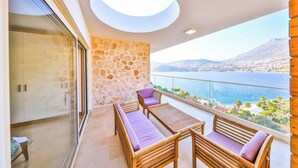 Ein Balkon mit Steinmauer, Holzmöbeln und Blick auf das Meer und die Berge.
