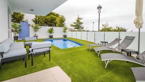 A rooftop pool area with artificial grass, lounge chairs, and a blue pool.