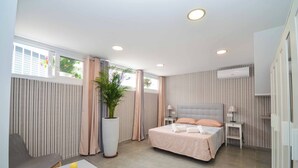 A modern bedroom with a large bed, a bedside table, a chair, a potted plant, and a window with curtains.