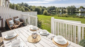A wooden deck with a table set for dining, overlooking a lake and greenery. - Windrush Lake 87, The Retreat (P) - Lakeside Lodge, On-site Facilities, Sleeps 6 (South Cerney)
