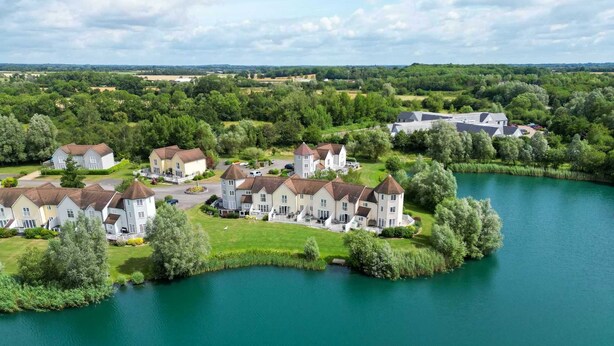 A lakeside property with multiple houses, a tower, and a large building, surrounded by lush greenery and a calm lake. - Windrush Lake 87, The Retreat (P) - Lakeside Lodge, On-site Facilities, Sleeps 6 (South Cerney)
