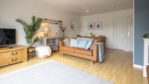 A cozy living room with a wooden floor, a brown leather sofa, a white rug, and a television on a wooden cabinet. - Windrush Lake 87, The Retreat (P) - Lakeside Lodge, On-site Facilities, Sleeps 6 (South Cerney)