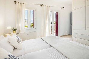 A bedroom with a bed, a nightstand, a lamp, a window with curtains, and a view of the outdoors. - Villa Marina Ai Helis (Ionian Islands)
