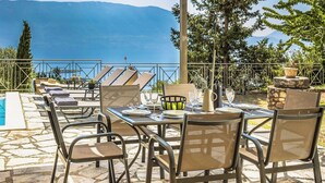 An outdoor dining area with a pool, chairs, and a table set for two, overlooking a scenic view.