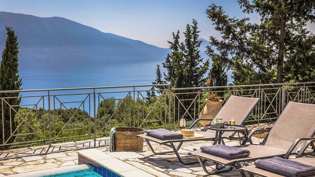 A poolside area with lounge chairs and a view of the sea and mountains.