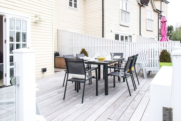 Una terraza con una mesa y sillas, una cerca blanca y un edificio al fondo.